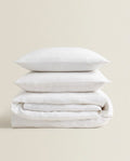 Two white pillows stacked on top of a folded white bedding set against a solid beige background.